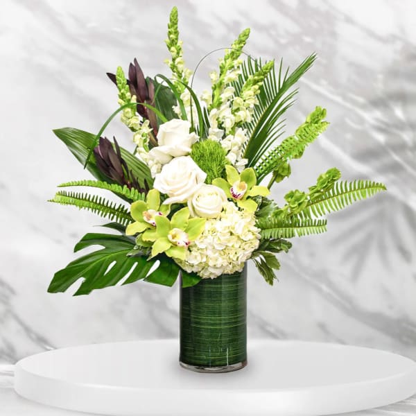White roses and green orchids in a tall glass vase