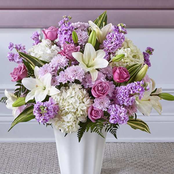 Tall arrangement of white lilies, pink roses, and lavender flowers in a white vase