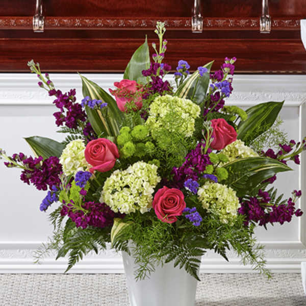 Tall arrangement of pink roses, green hydrangeas and purple flowers in a white container