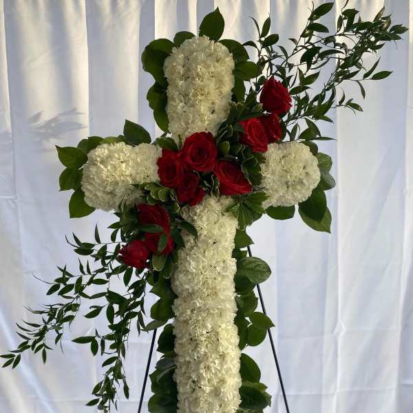 Tall white floral cross with red roses and greenery displayed on a metal easel