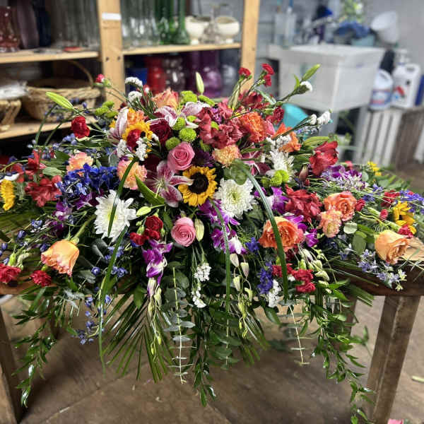 Large multicolored spray of mixed flowers cascading across a wooden table.