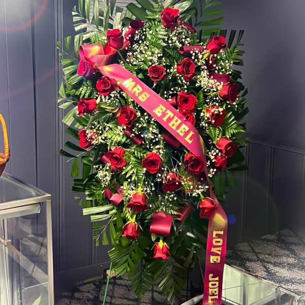 Standing spray of red roses with a pink ribbon and greenery