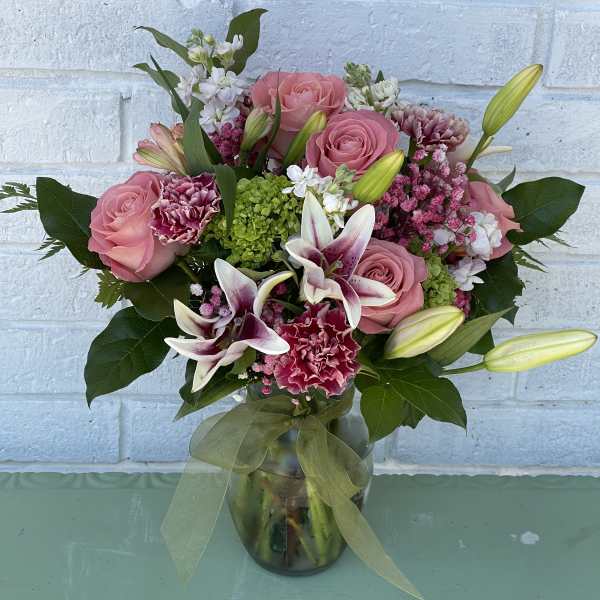 Pink roses and lilies arranged in a glass vase with a ribbon