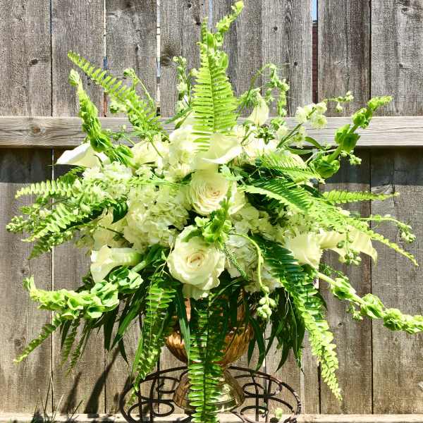 Large white rose and hydrangea arrangement with ferns in a gold urn on a metal stand