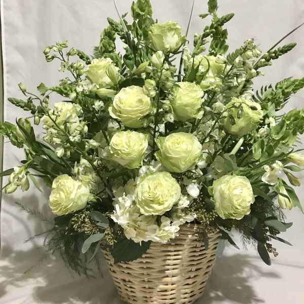 Tall basket arrangement of pale green and white flowers with roses and hydrangeas.