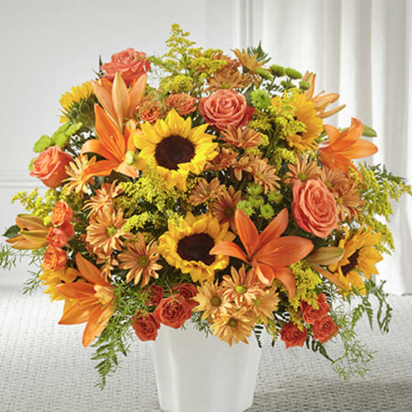 Large orange and yellow arrangement with sunflowers, lilies, roses, and mums in a white vase