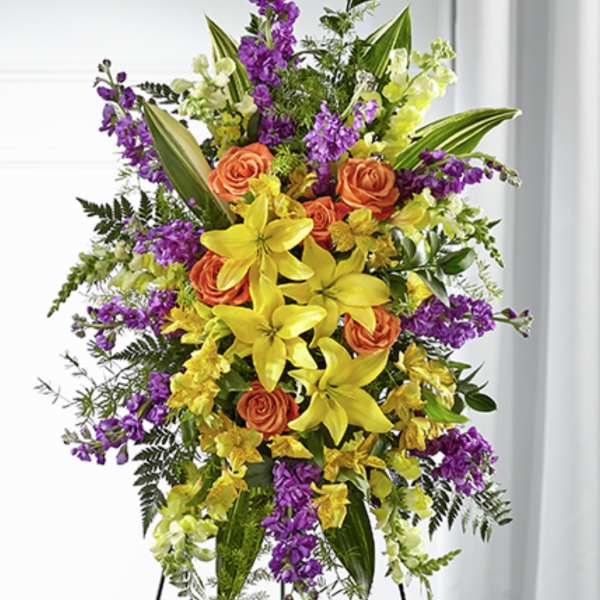 Tall standing spray of yellow lilies, orange roses, and purple flowers on a metal easel