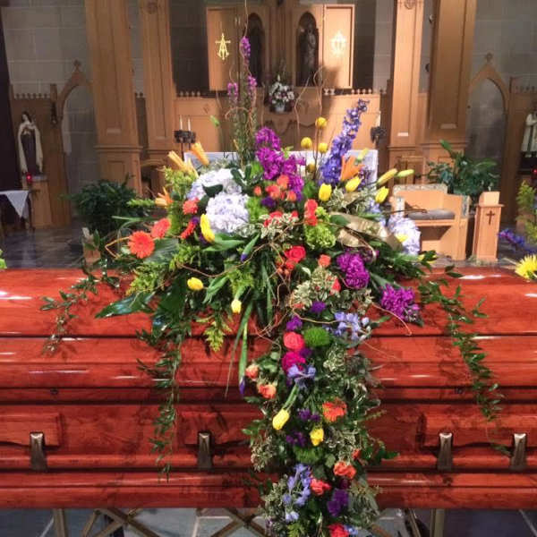 Large colorful floral cross displayed on a casket in a church