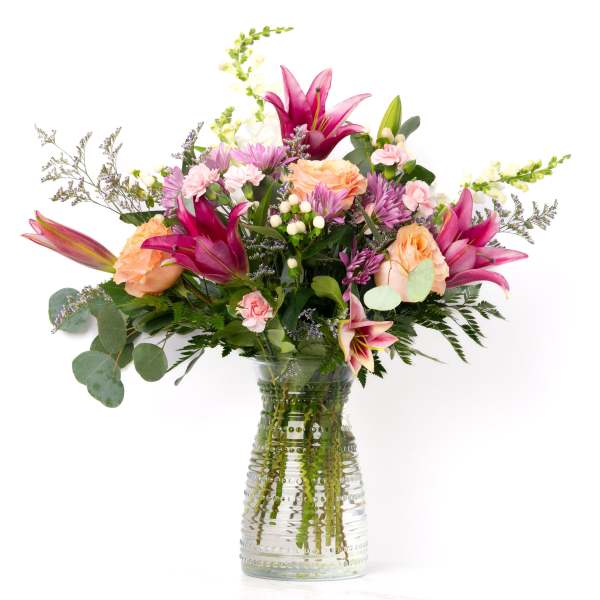 Mixed bouquet of pink lilies, peach roses, and pastel blooms in a clear textured glass vase