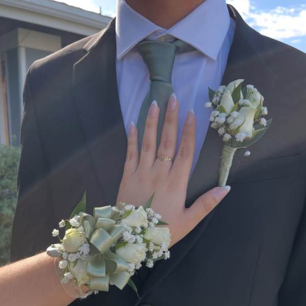 White boutonniere and wrist corsage with pale green ribbon on formalwear