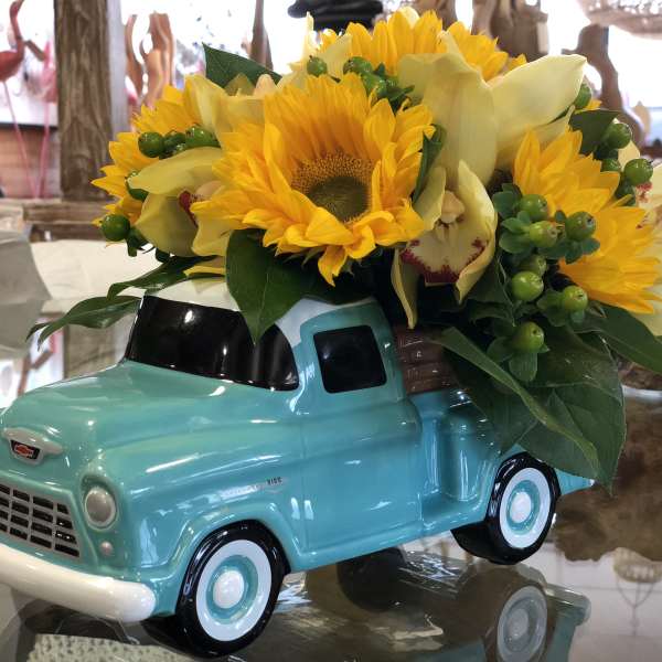 Sunflowers and pale yellow orchids arranged in a turquoise truck planter