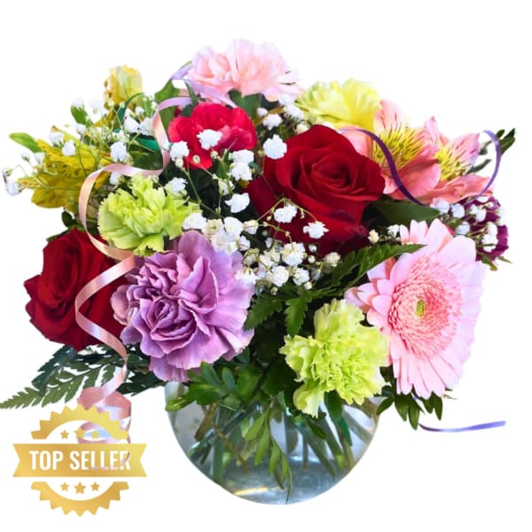 Mixed bouquet of roses, carnations, and gerbera daisies in a glass vase