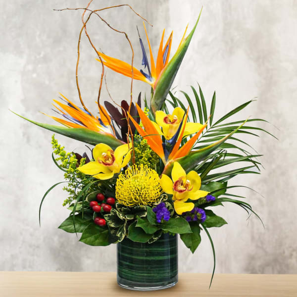 Tropical flower arrangement with yellow orchids and bird-of-paradise in a glass vase