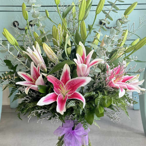Pink stargazer lilies in a glass vase with a purple ribbon