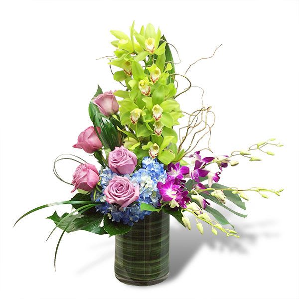 Tall modern arrangement with green orchids, pink roses, blue hydrangea, and purple orchids in a green vase