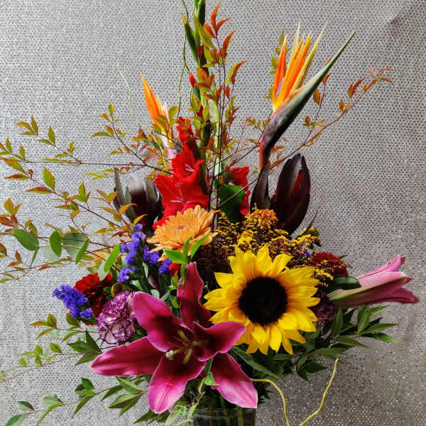 Tall mixed bouquet with sunflowers, lilies, and tropical blooms in a glass vase