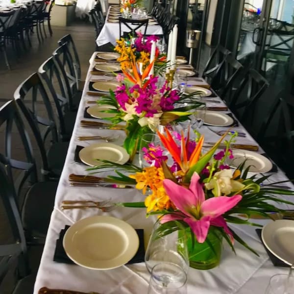 Tropical floral centerpieces on a long banquet table with plates and candles