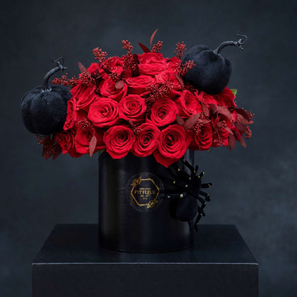 Red roses arranged in a black vase with black pumpkin accents