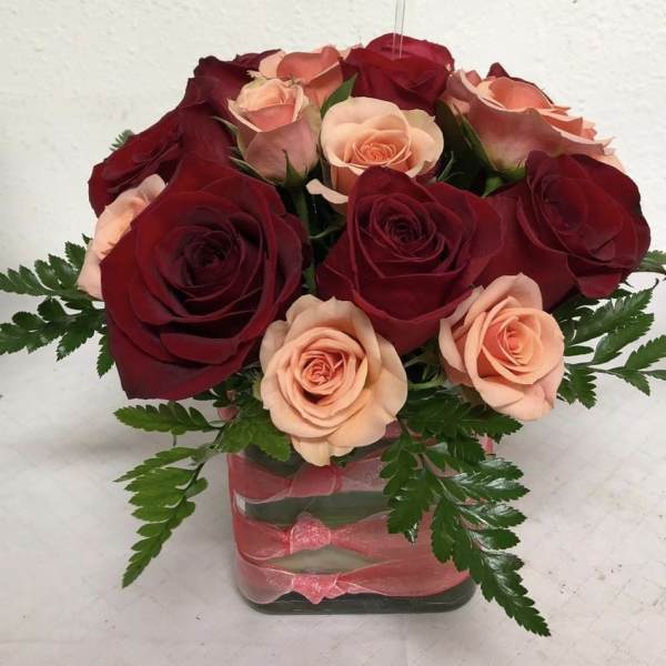 Bouquet of red and peach roses in a square glass vase with pink ribbon