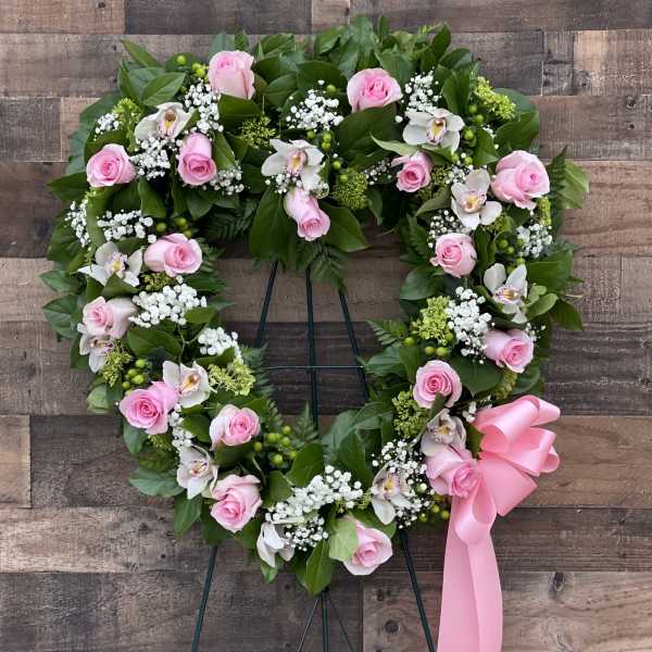 Heart-shaped floral wreath with pink roses and white orchids on a stand