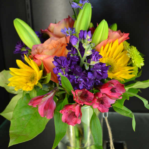 Colorful bouquet of lilies, sunflowers, and purple flowers in a glass vase