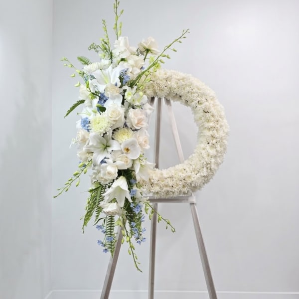 White floral wreath on an easel with a cascading bouquet of white blooms