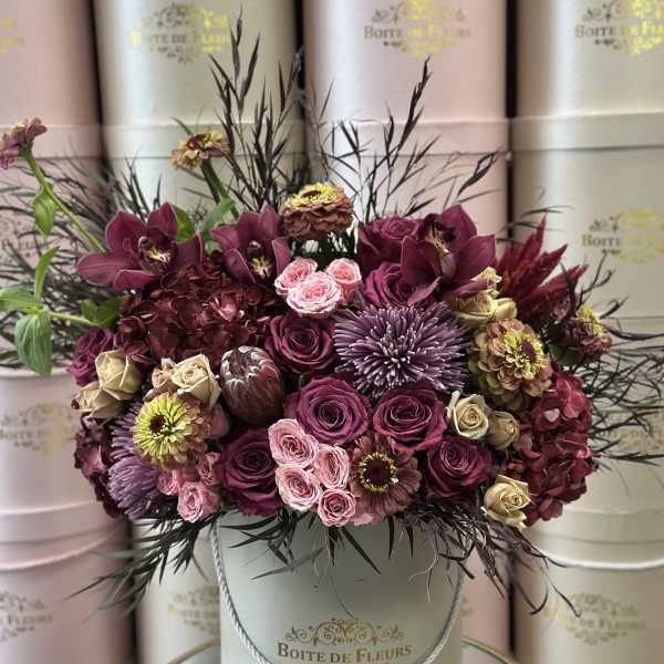A burgundy and pink floral arrangement in a round hatbox.