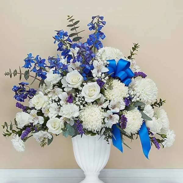White and blue floral arrangement in a white urn vase with ribbon