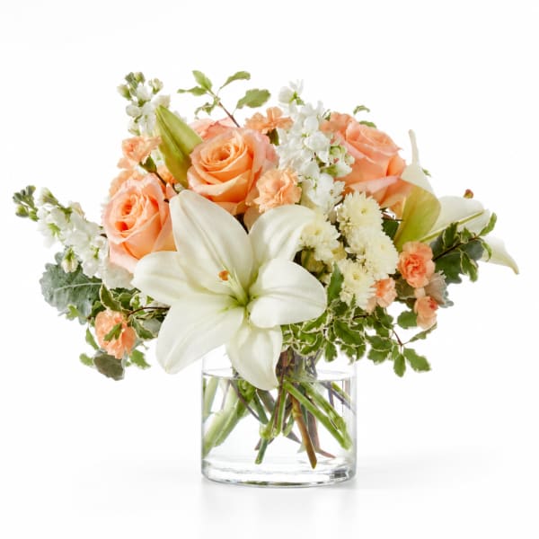 Peach roses and white lilies in a clear glass vase