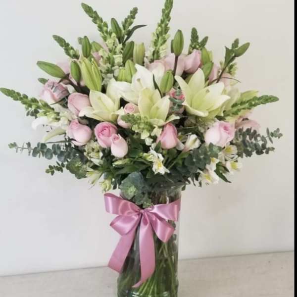 Pink and white bouquet of lilies and roses in a glass vase with a pink ribbon