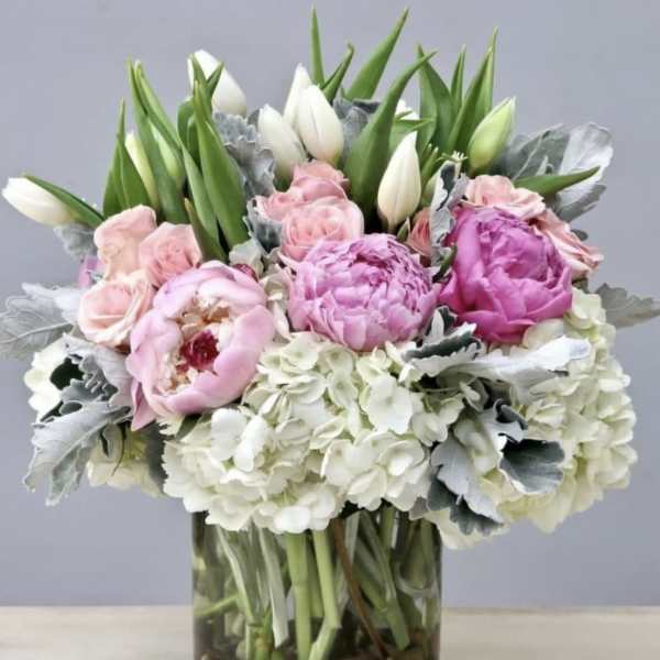 Pink peonies and white tulips in a glass vase with hydrangeas