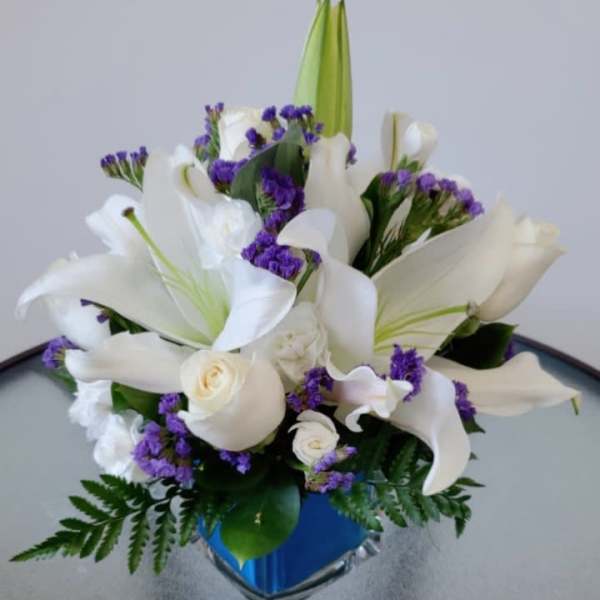 White lilies and purple filler flowers arranged in a blue vase