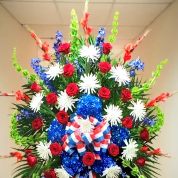 Patriotic standing spray of red roses, white mums, and blue accents with striped bow on an easel