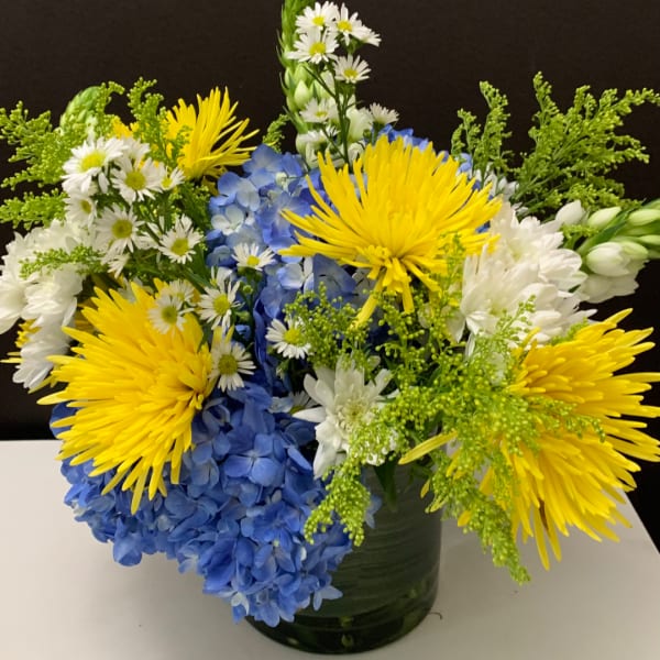 Yellow and white flowers with blue hydrangeas in a green vase