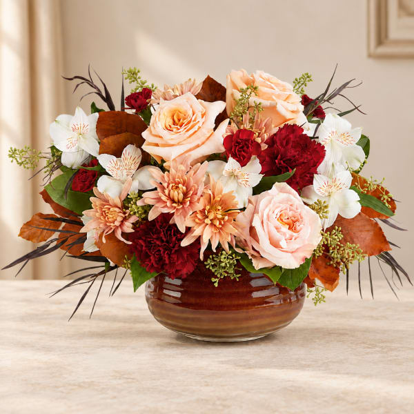 Peach and red floral arrangement in a brown glass bowl vase