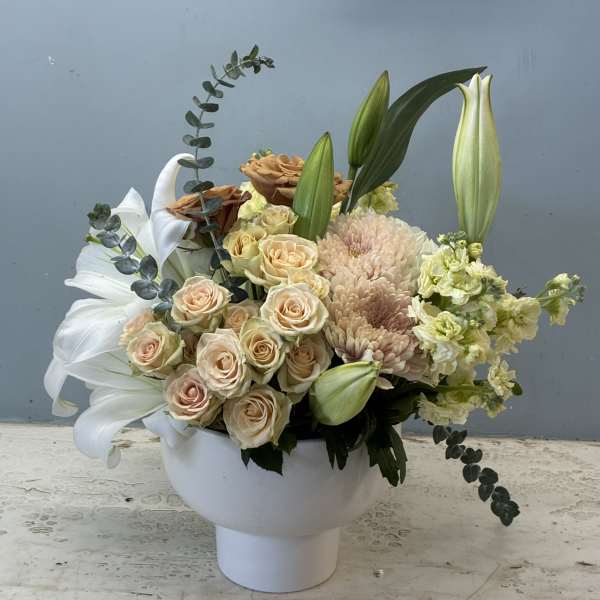 Cream roses and lilies arranged in a white pedestal vase