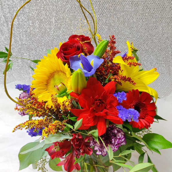 Bright mixed bouquet with red roses, sunflowers, and lilies in a glass vase