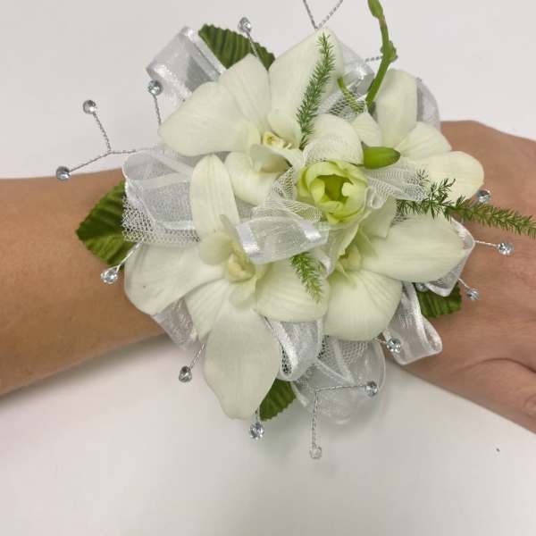 White orchid wrist corsage with silver ribbon and beaded accents on a hand
