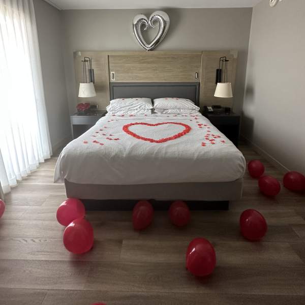 Bedroom decorated with a heart made of red petals on the bed and red balloons on the floor.