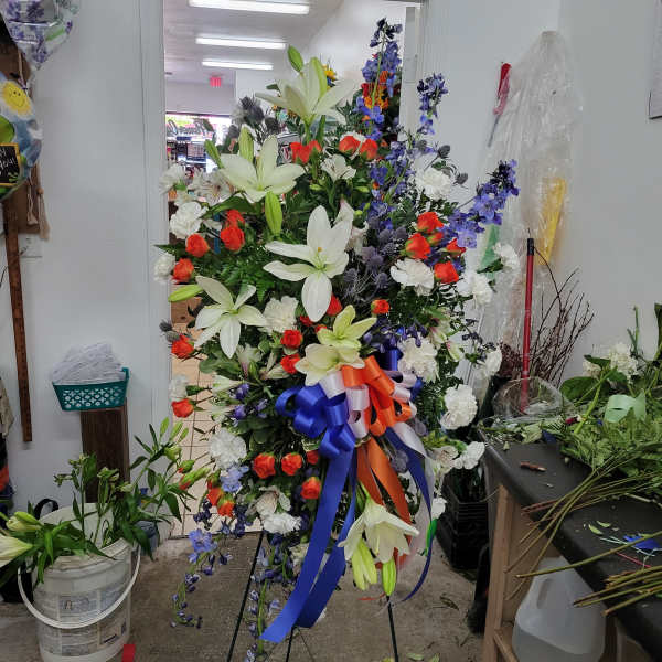 Large standing floral spray with white lilies, orange roses, and blue ribbon