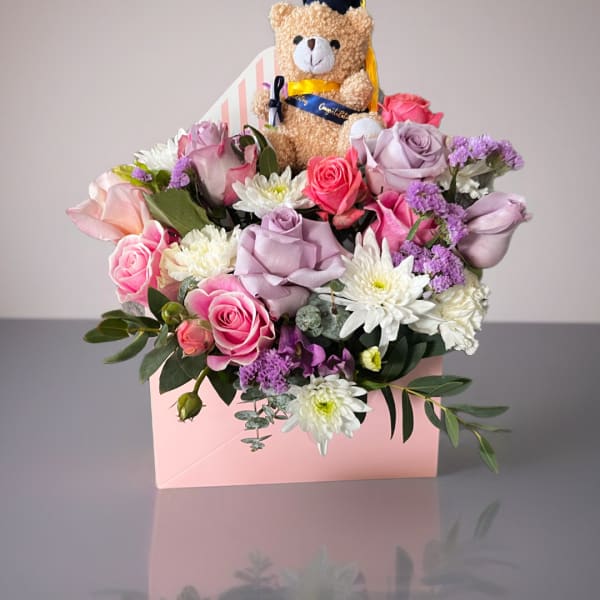 Pink and lavender roses with white mums in a pink box, topped with a teddy bear