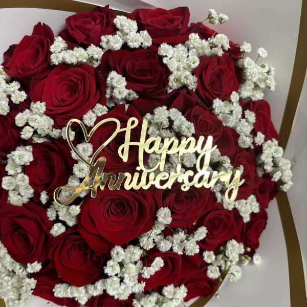 Red roses with white baby's breath and a gold Happy Anniversary topper