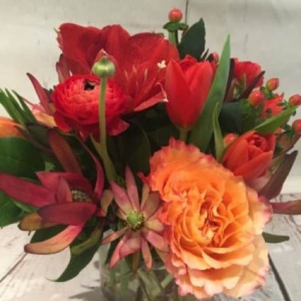 Compact red and orange flower arrangement in a clear glass cylinder vase