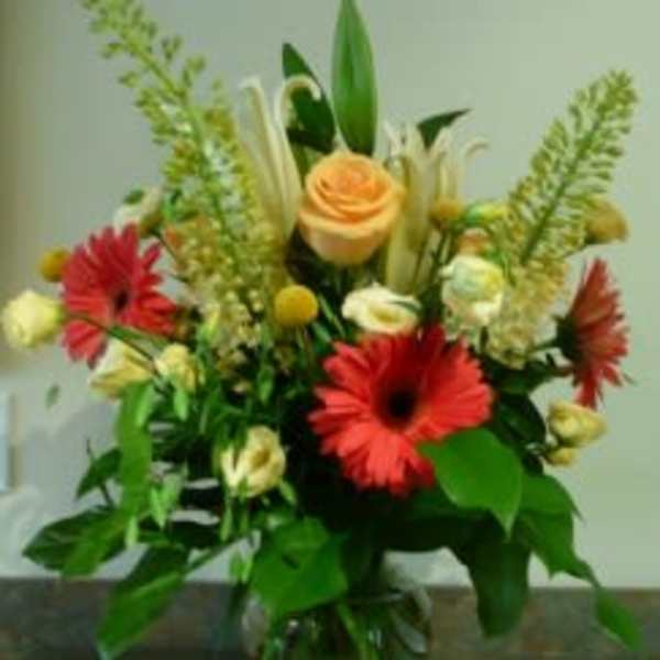 Mixed arrangement with red gerbera daisies, a peach rose, and cream flowers in a clear glass vase