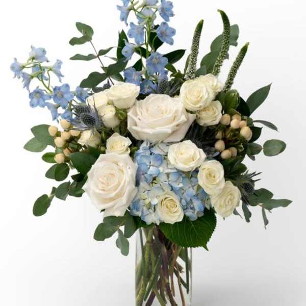 White roses and blue hydrangea with blue delphinium in a clear glass vase