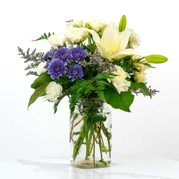 White lilies and purple daisies in a glass jar vase