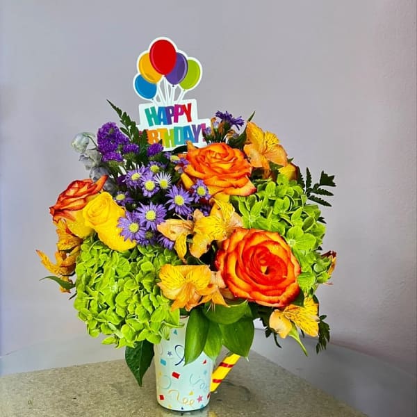 Birthday bouquet with roses, hydrangea, and a balloon topper in a decorated cup