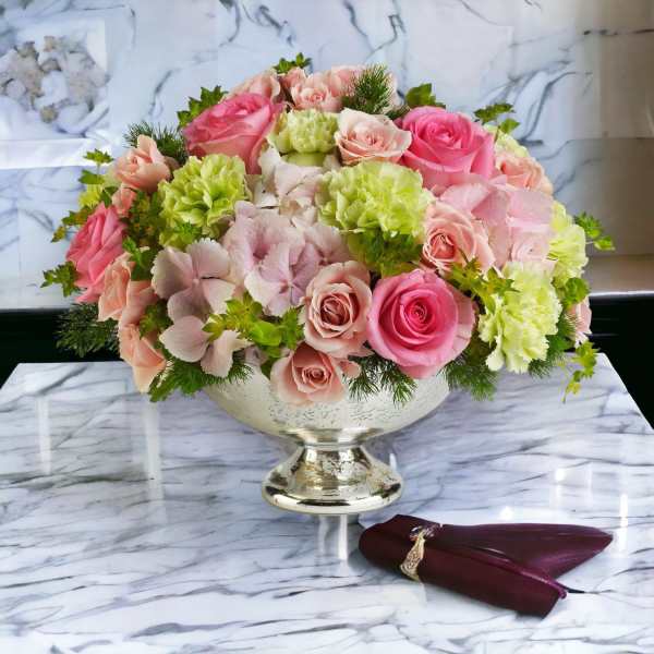 Low arrangement of pink roses, pale hydrangeas, and green carnations in a silver compote vase