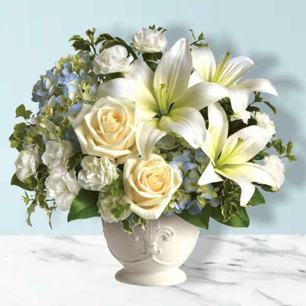 White lilies and cream roses in a white vase with blue hydrangeas