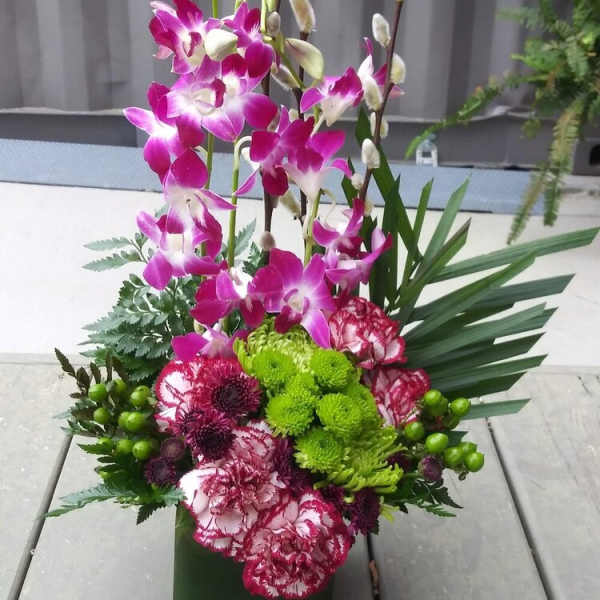 Tall orchid and carnation arrangement in a dark green container